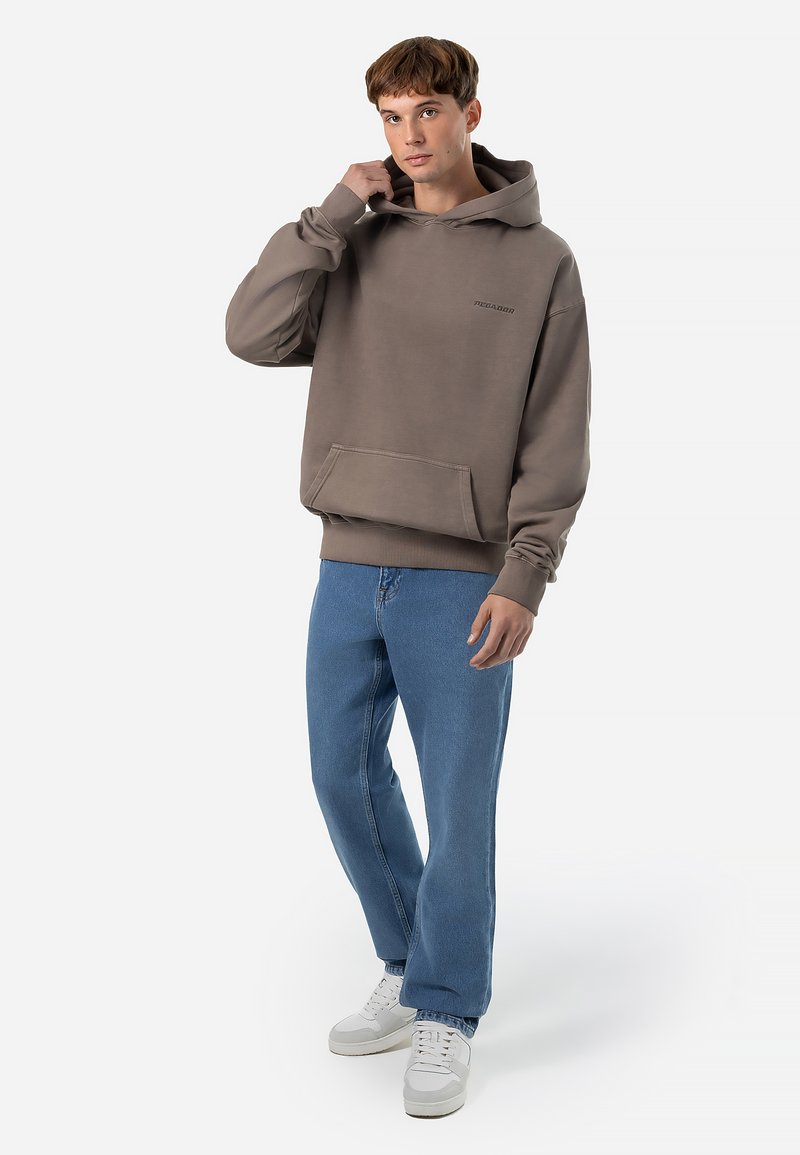 Bruine hoodie van een katoenmix met een kangoeroezak en geribde mouwen. Gecombineerd met blauwe jeans en witte sneakers, staande op een effen achtergrond.
