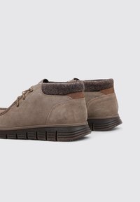 Zapatos de ante marrón con un cuello de tela marrón acolchada y acentos en marrón, que cuentan con una suela de goma texturizada y un diseño con cordones.