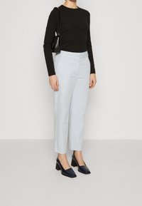 Svart långärmad topp, ljusblå högmidjade byxor, svart handväska, och marinblå klackskor med fyrkantig tådesign.