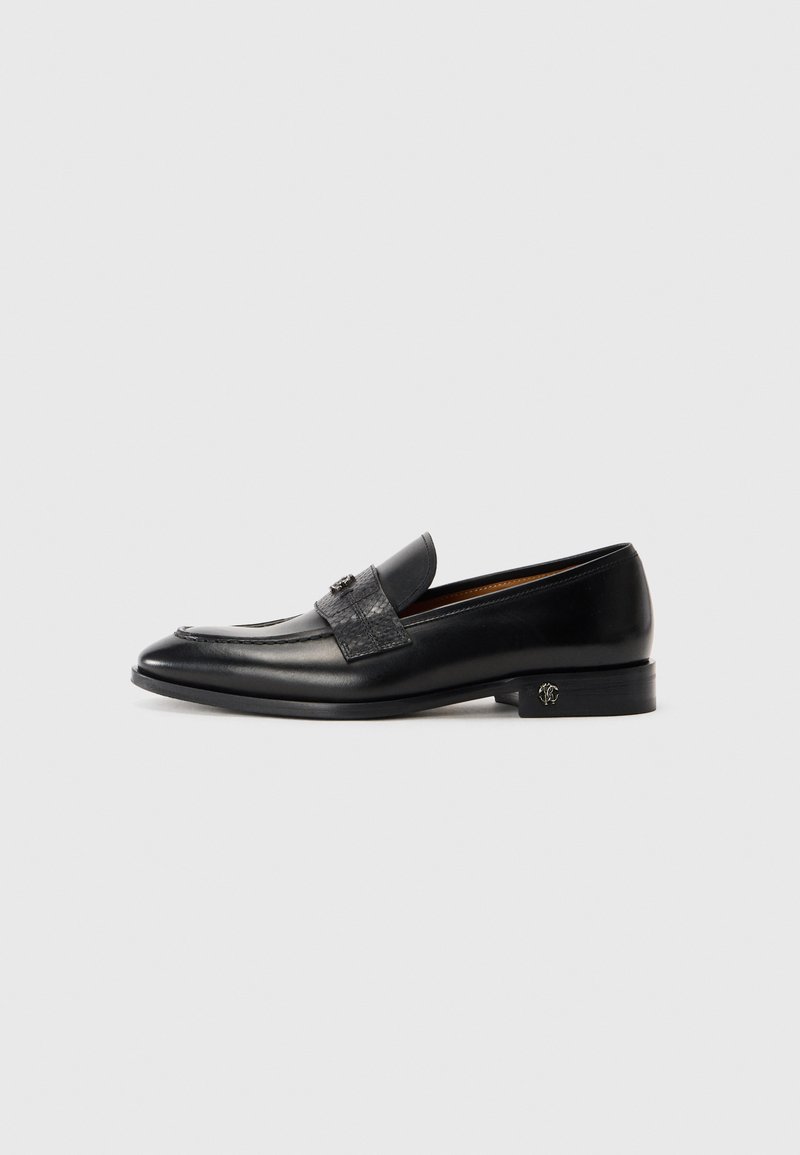 Svarta läder herrloafers med ett dekorativt rem och låg klack som har ett litet metallemblem på sidan.