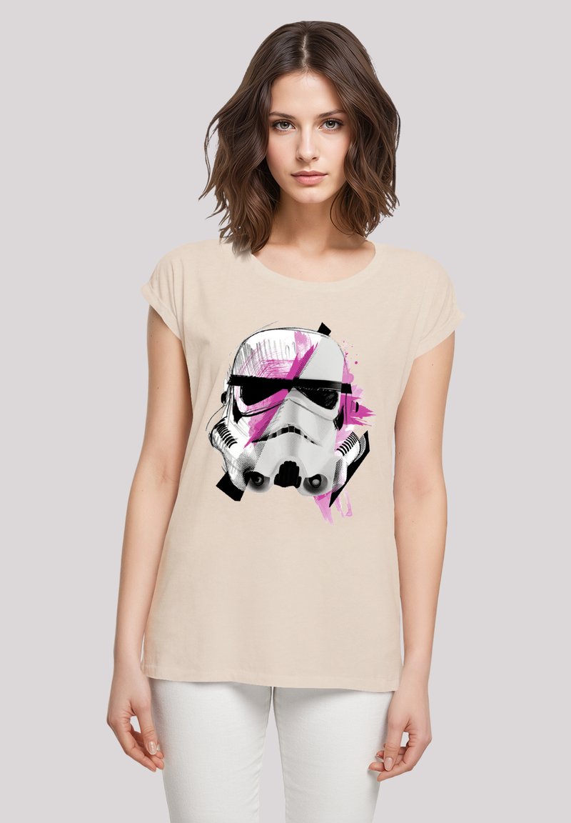 Beige t-shirt with short sleeves featuring a graphic of a Stormtrooper helmet. Design includes black outlines and pink paint splashes.
