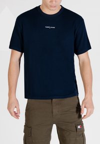 T-shirt in cotone blu navy con maniche corte, scollo rotondo e logo "TOMMY JEANS" ricamato sul petto. Vestibilità casual, texture liscia.