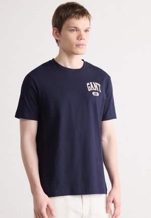 Camiseta de algodón azul marino de manga corta. Presenta un logo impreso con el texto "GANT" y "49" en el pecho en un color contrastante.
