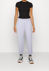 Černé přiléhavé tričko s krátkým rukávem v kombinaci se světlými levandulovými tepláky s elastickým pasem a vyšitými detaily, nošeno s černými vysokými teniskami.