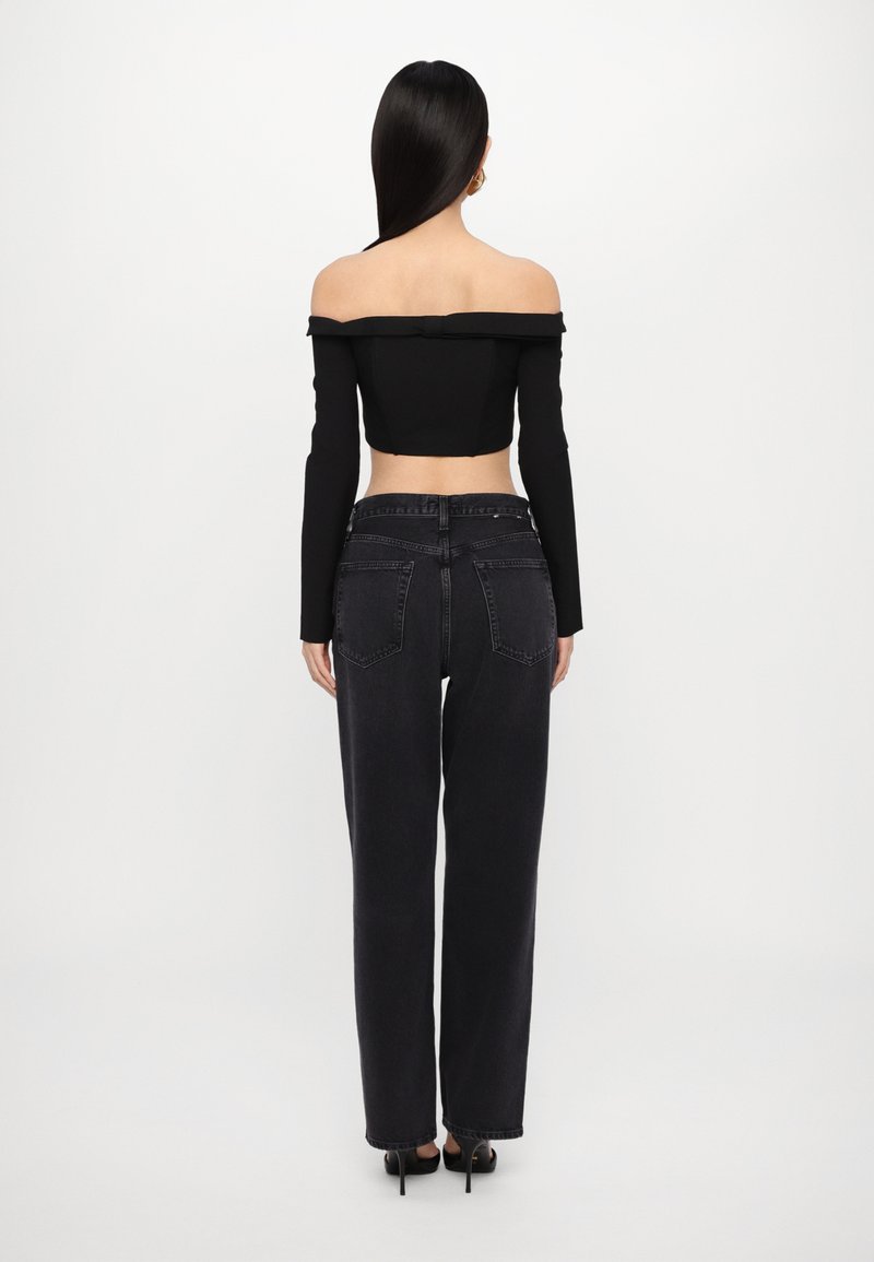 Haut noir à épaules dénudées avec manches longues, associé à un jean noir ample taille haute. Texture lisse, design minimaliste, sans motifs visibles.