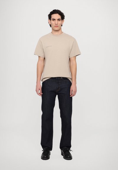 Beige Baumwoll-T-Shirt mit lockerer Passform, kurzen Ärmeln und grafischem Detail. Dunkelblaue Jeans aus Denim, gerader Schnitt, mit dezenten Nähten und Taschen.