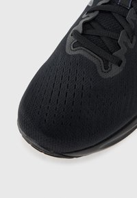 Zapatilla deportiva negra con un upper de punto texturizado y agujeros de ventilación, cordones negros planos y una suela de goma lisa.