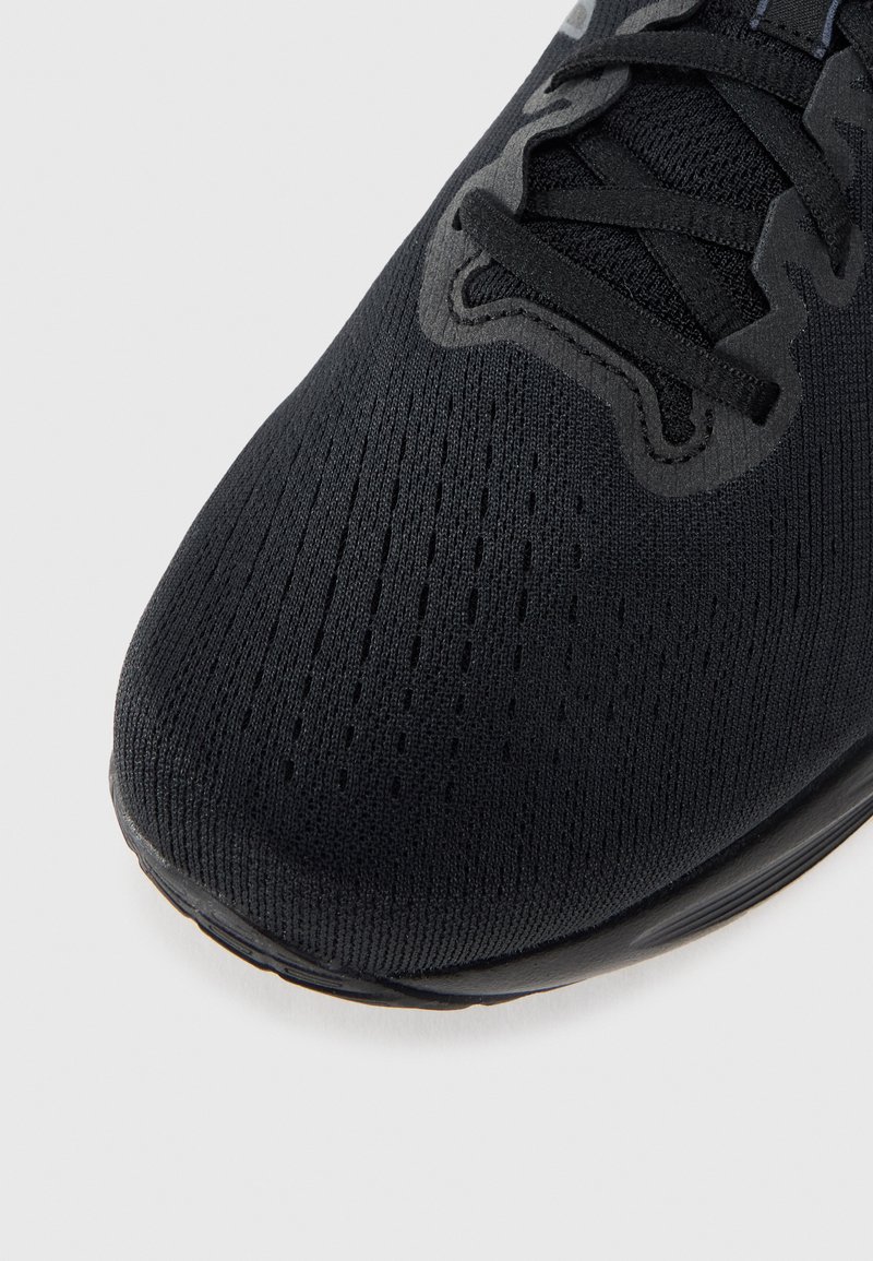 Schwarzer Sportschuh mit einer strukturierten, gestrickten Oberseite mit Belüftungsöffnungen, flachen schwarzen Schnürsenkeln und einer glatten Gummisohle.