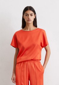 Red silk t-shirt with a relaxed fit, dropped shoulders, and a wide neckline. Paired with matching elastic-waist trousers. Smooth texture.