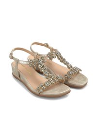 Sandali con tacco a cuneo beige con design a T, arricchiti da accenti simili a gemme trasparenti, con una morbida lucentezza metallizzata e una cinghia alla caviglia regolabile.