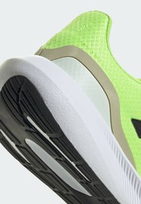 Scarpa sportiva verde con tomaia in maglia texturizzata, accenti beige a contrasto e suola bianca con motivi in gomma nera.
