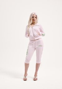 Rózsaszín cipzáras kapucnis pulóver zöld felirattal, hozzá illő, zöld feliratos, rövidített szárú melegítőnadrággal. Puha anyag és húzózsinór részletek.