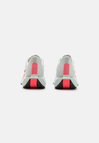 Grijze sport schoenen met roze accenten, voorzien van een gestructureerde bovenkant en een contrasterende zwarte en rode zool. Zicht van achteren.
