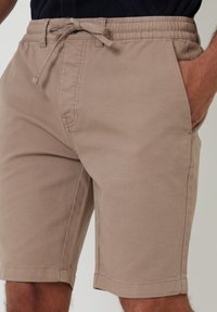 Shorts en coton beige avec une taille élastique et un cordon de serrage, dotés de deux poches latérales et d'une coupe droite et épurée. Tissu léger.