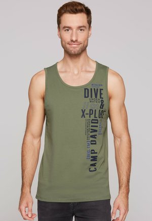 Mann in olivgrünem ärmellosem Shirt mit marineblauem Text "Tauche unter Wasser & erkunde Camp David" auf der Vorderseite vor einem einfarbigen Hintergrund.
