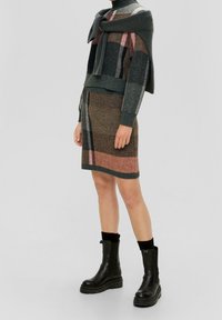 Stickad tröja med en viken krage i grå nyanser, ihopparad med en mönstrad stickad kjol med bruna, rosa och grå ränder. Svarta anklarstövlar.