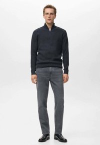 Maglione blu scuro a maglia con scollatura a mezza zip, abbinato a jeans grigi a gamba dritta e scarpe nere in pelle. Design semplice e texturizzato.