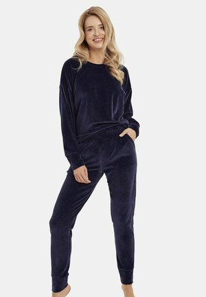Granatowy welurowy komplet do noszenia w domu składający się z luźnej bluzki z długim rękawem i spodni z elastycznym paskiem. Gładka tekstura oraz dopasowane ściągacze przy kostkach.