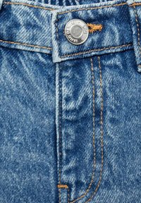 Jeans i denim med en ljusblå färg, synlig sömnad i kontrasterande orange, metallknäppning och en lätt distressed textur.