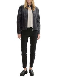 Veste en cuir noir avec fermeture éclair, texture côtelée sur les côtés, associée à un pull beige, un pantalon noir ajusté et des mocassins noirs.