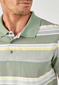 Polo shirt in groen met horizontale strepen in wit en geel. Voorzien van een kraag, drie knopen en een borstzak. Textuurstof.
