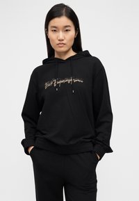 Μαύρο φούτερ με κουκούλα από βαμβακερό μείγμα, με μεταλλικό χρυσό γραφικό στο μπροστινό μέρος, άνετη εφαρμογή και μανσέτες και τελείωμα με ριμπ ύφανση.