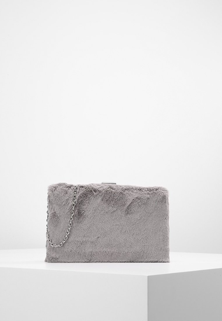 Pochette rectangulaire grise avec une texture douce en fourrure et une bandoulière chaîne argentée, placée sur une surface blanche sur un fond uni.