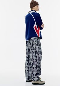 Plavi i crveni pleteni pulover s geometrijskim uzorkom, uparen sa sivim širokim hlačama s uzorcima koji sadrže tamne motive. Svijetle čizme.