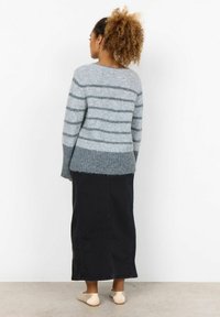 Grijs gestreepte gebreide trui met een zachte textuur, gecombineerd met een lange zwarte denim rok en lichtbeige instappers.