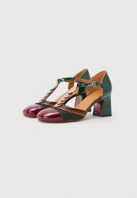 Leather heeled shoes with a T-strap design. Colors include burgundy, black, and green, with a glossy finish and textured fabric accents.