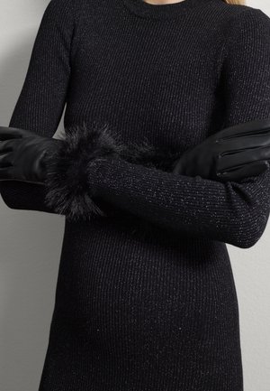 Zwarte geribbelde trui met metallic draden, voorzien van lange mouwen en een zwarte neplederen manchet, gecombineerd met elegante zwarte leren handschoenen.
