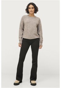 Maglione lavorato a maglia di un marrone chiaro con finiture a coste, abbinato a pantaloni svasati neri e stivaletti beige con suola spessa. Sfondo semplice.