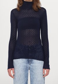 Top a maniche lunghe con collo alto di colore blu navy, con un design a maglia aperta e testurizzato che presenta motivi a diamante e una silhouette aderente.