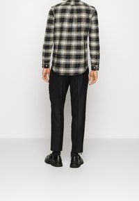 Czarna i biała koszula w kratę z długim rękawem i kołnierzykiem na guziki, zestawiona z czarnymi spodniami i czarnymi butami, widziana od tyłu.