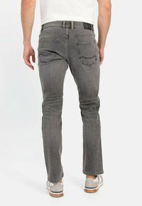 Harmaat farkut slim fit -leikkauksella, joissa on kaksi takataskua ja musta brändilogo vyötäröllä, yhdistettynä beigeihin tennareihin.