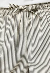 Pantalon de pyjama blanc avec fines rayures verticales noires et taille à cordon noué.