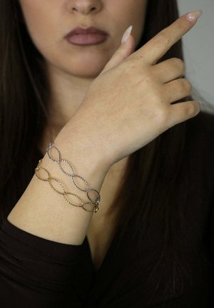 Bracelet en maillons torsadés argent et or porté au poignet, présentant un design alterné avec une finition lisse et une apparence légère.