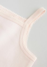 Miękka, różowa tkanina zbliżenie przedstawiające ramiączko i dekolt wykończone koronką na lekkim ubraniu.