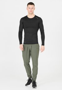 Zwart langengemouwde sporttop met een gestructureerd patroon, gecombineerd met licht olijfgroene tapered broek en zwarte sportschoenen.