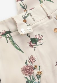 Lichtbeige stof met bloempatronen in roze, geel en groen. Voorzien van metalen hardware en een op maat gemaakte tailleband.
