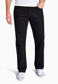 Schwarze Jeans im Straight-Leg-Schnitt, mit vier Taschen und klassischem Design. Kombiniert mit weißen Sneakern, was einen lässigen Look unterstreicht.