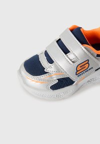 Child's navy and silver Skechers sneaker with orange lining, two Velcro straps, and textured white sole on a white background.