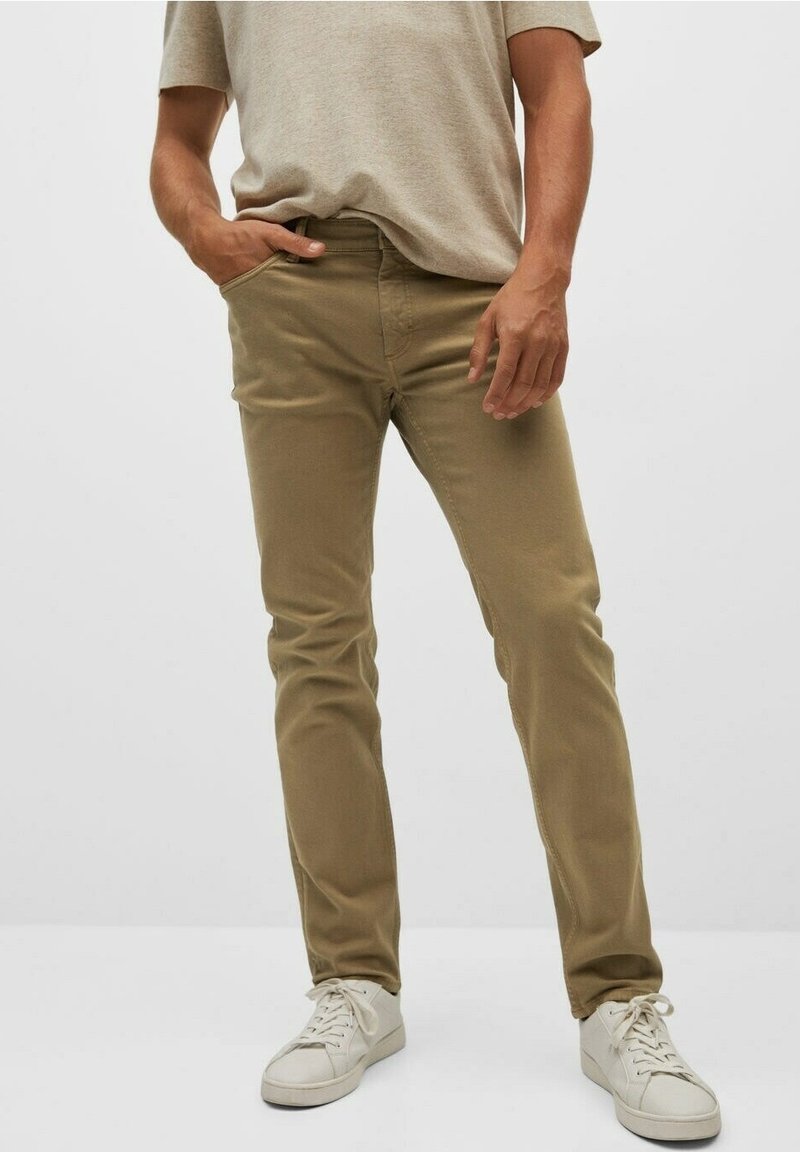 Chinos en coton beige avec une coupe slim, dotés de poches avant, d'un zip et d'une texture subtile, associés à des baskets blanches.