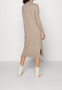 Robe en maille beige avec un col montant, des manches longues et des fentes latérales, associée à des bottines crème. Texture lisse et coupe mi-longue.