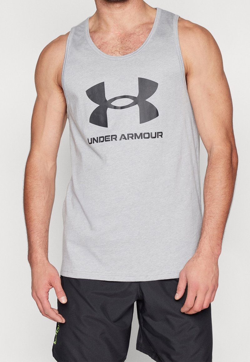 Débardeur gris clair avec un logo Under Armour noir traversant la poitrine, fabriqué dans un tissu doux. Associé à un short noir.