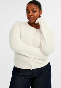 Vit cardigan med rund halsringning, med knappstängning och långärmar. Mjuk, strukturerad tyg kombinerad med mörk denimjeans.