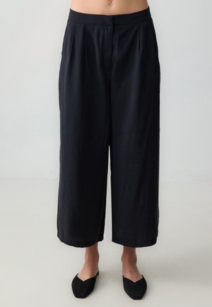 Pantalons larges noirs en tissu léger avec des plis à l'avant, dotés d'une taille haute et d'un ourlet net.
