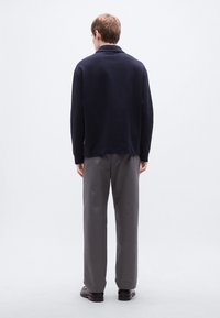 Μπλε ναυτικό πουλόβερ με γιακά, συνδυασμένο με γκρι παντελόνι. Το σύνολο διαθέτει άνετη εφαρμογή και μαλακή υφή υφάσματος.