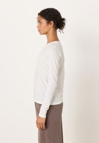 Valge pika varrukaga särk, mis on valmistatud kerge kangaga, ümmarguse kaelusega, veidi läbipaistva tekstuuriga, randmetel istuv, sobitatuna halli alaosaga.