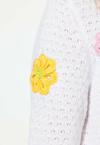 Maglione bianco lavorato a maglia con un motivo testurizzato, caratterizzato da fiori ricamati gialli e rosa sulle maniche.